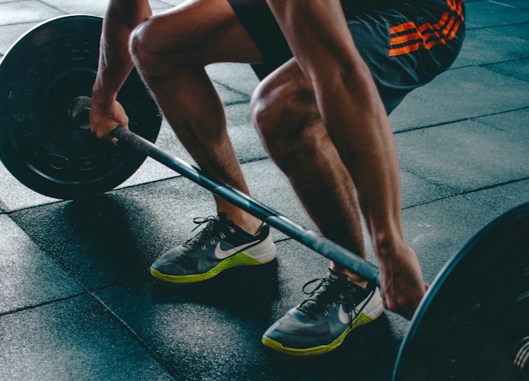 Person crouching on a gym floor and gripping a barbell before a weightlifting exercise